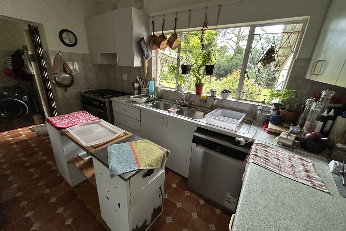 A dated kitchen featuring original cabinetry, a double sink, built-in stove, and large window overlooking the garden, offering potential for modernization.
