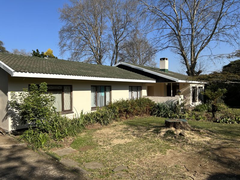 A single-story residential home featuring a tiled roof, chimney, and established garden setting with a front lawn and driveway access.