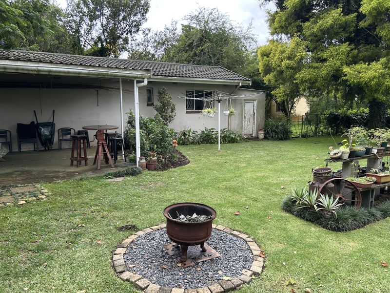 A spacious rear garden featuring a covered patio area, a central fire pit with stone surround, and established lawn and greenery.