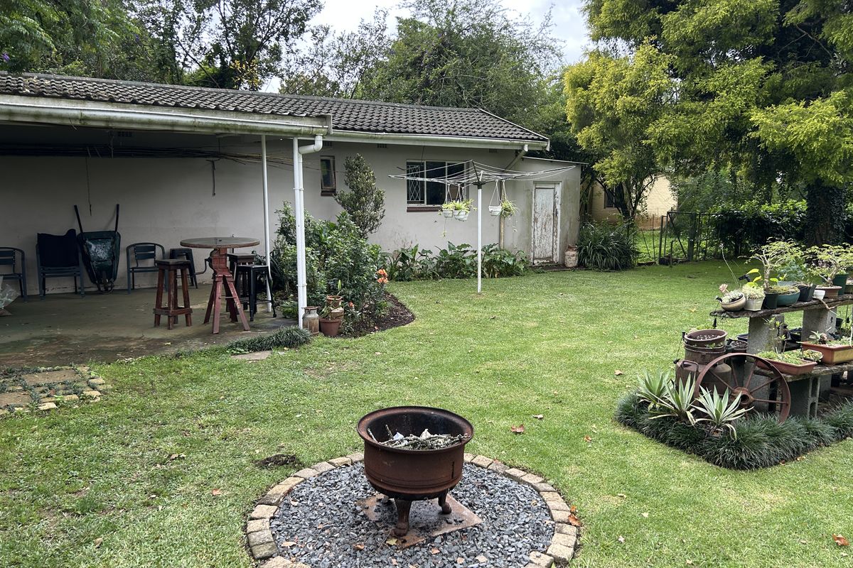 A spacious rear garden featuring a covered patio area, a central fire pit with stone surround, and established lawn and greenery.