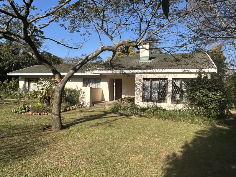 A single-story residential house featuring a tiled roof, chimney, and diamond-patterned window security bars, set within a mature garden.