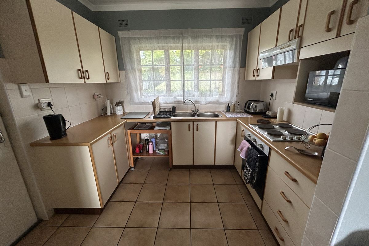A functional kitchen featuring laminate countertops, built-in cabinetry, a double bowl sink, and integrated electric cooking appliances with tiled flooring and backsplash.