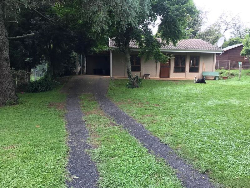 Front view of a single-story brick house featuring a tiled roof, attached garage, and a gravel driveway set within a spacious garden.