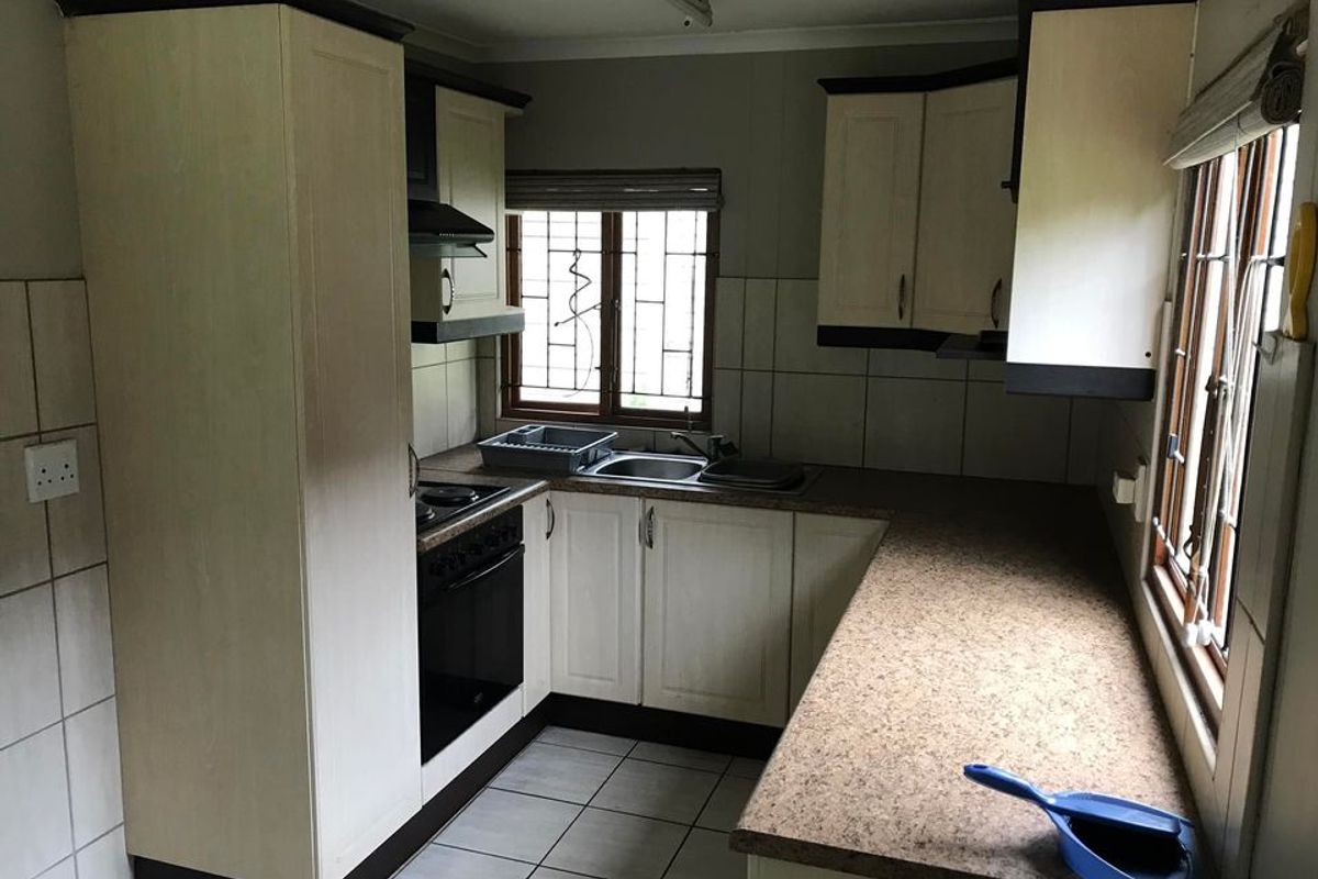 A functional kitchen featuring built-in cabinetry, laminate countertops, a stainless steel sink, and integrated cooking appliances with tiled flooring and splashbacks.
