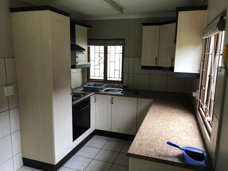 A functional kitchen featuring built-in cabinetry, laminate countertops, a stainless steel sink, and integrated cooking appliances with tiled flooring and splashbacks.