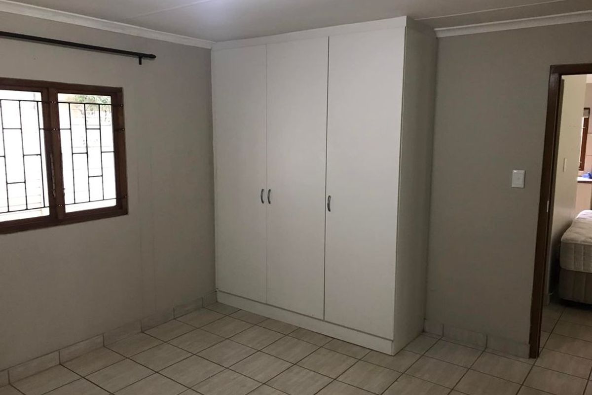 A clean, empty bedroom featuring neutral wall tones, tiled flooring, and a large white built-in wardrobe with security bars on the window.
