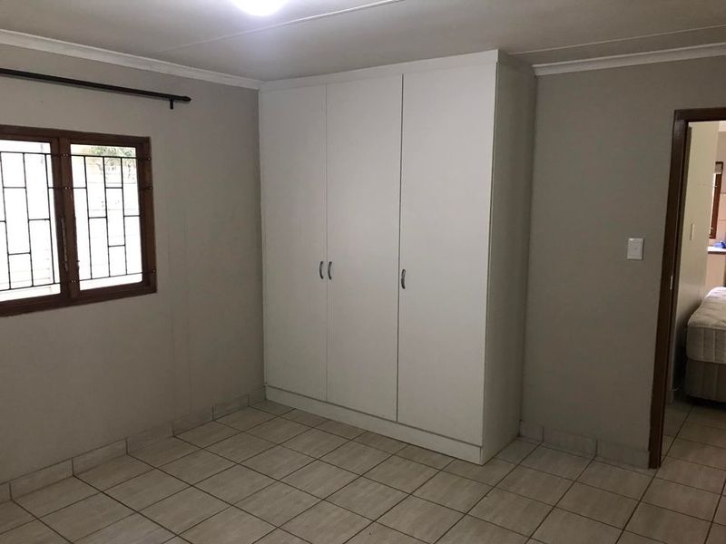 A clean, empty bedroom featuring neutral wall tones, tiled flooring, and a large white built-in wardrobe with security bars on the window.
