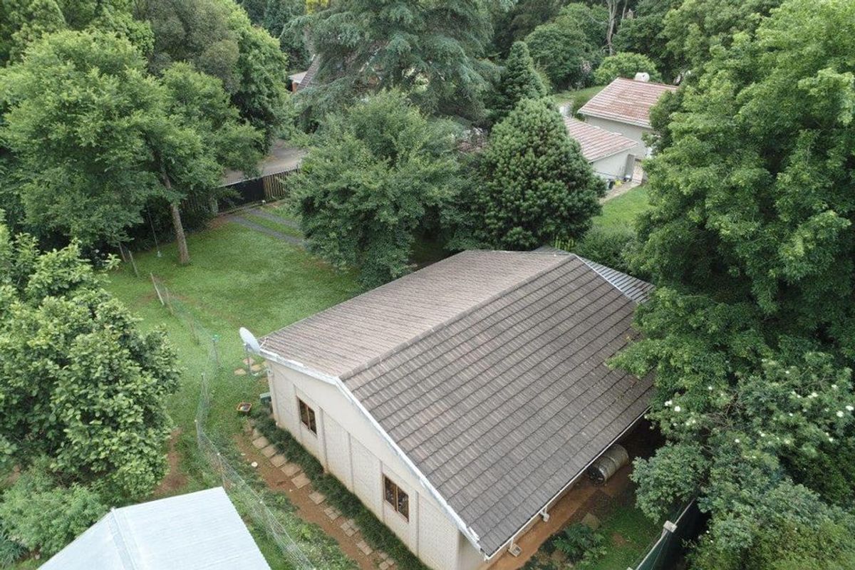 Aerial view of the property showing the tiled roof, surrounding garden, mature trees, and paved pathway access.