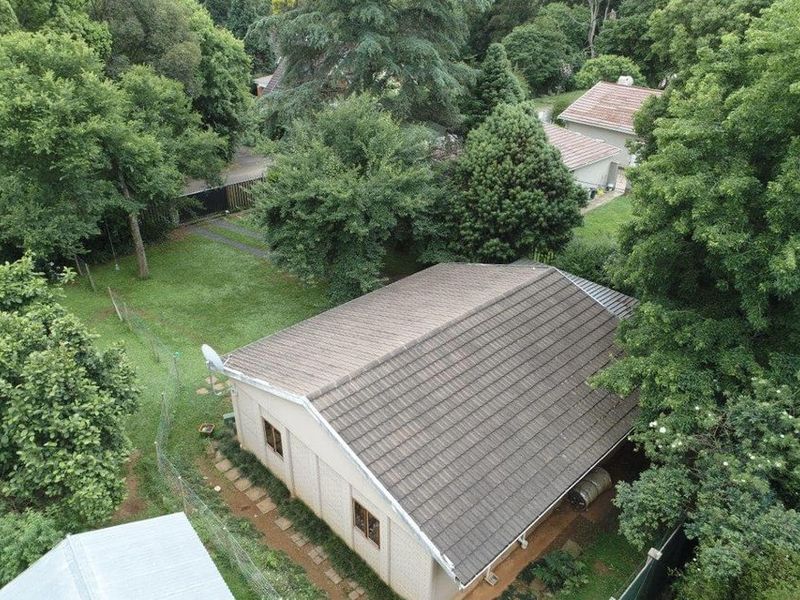Aerial view of the property showing the tiled roof, surrounding garden, mature trees, and paved pathway access.