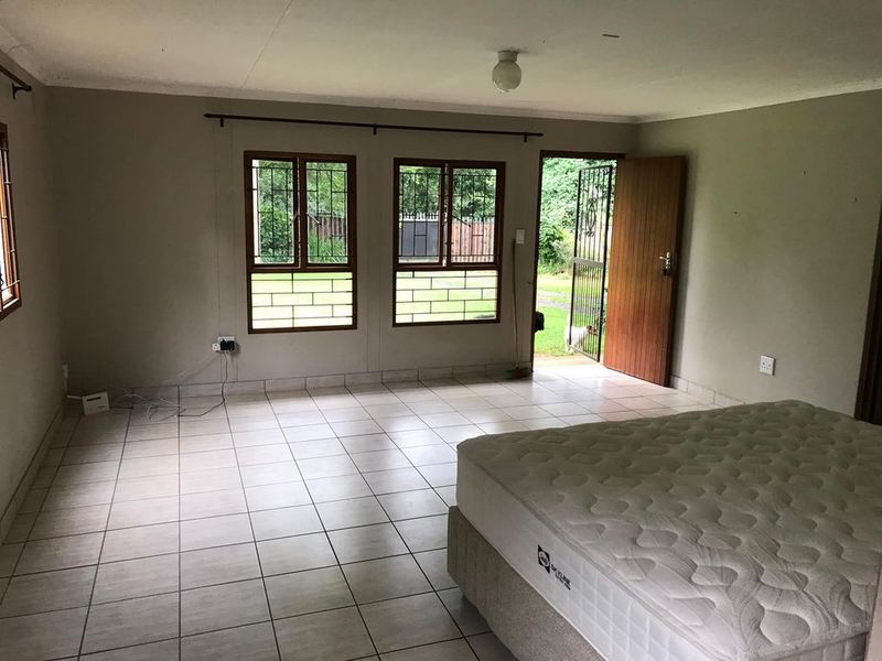 A bedroom featuring tiled flooring, security bars on the windows, and direct access to the exterior through a timber door.