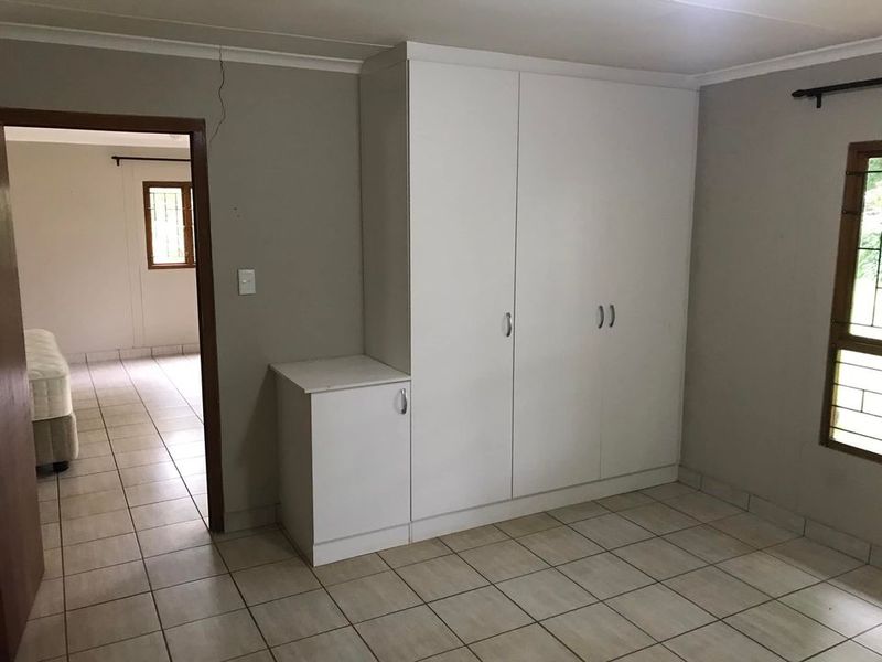 A bedroom featuring built-in white cupboards, tiled flooring, and security bars on the windows, with a view into an adjacent room.