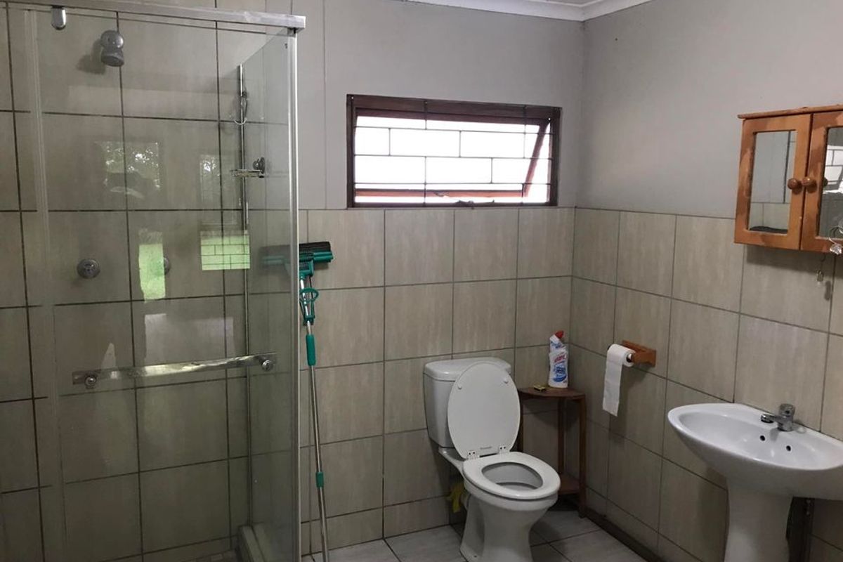 A functional bathroom featuring a glass-enclosed shower, pedestal basin, and toilet, finished with neutral wall and floor tiling.