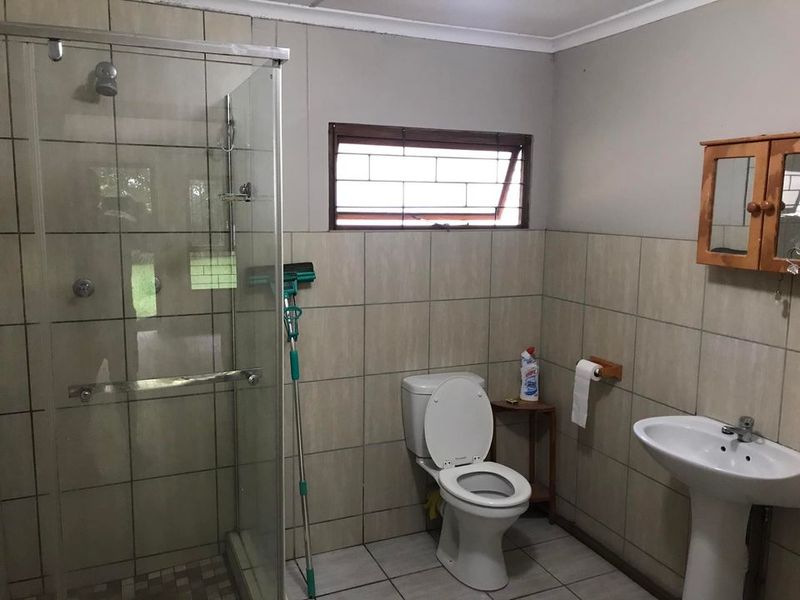 A functional bathroom featuring a glass-enclosed shower, pedestal basin, and toilet, finished with neutral wall and floor tiling.