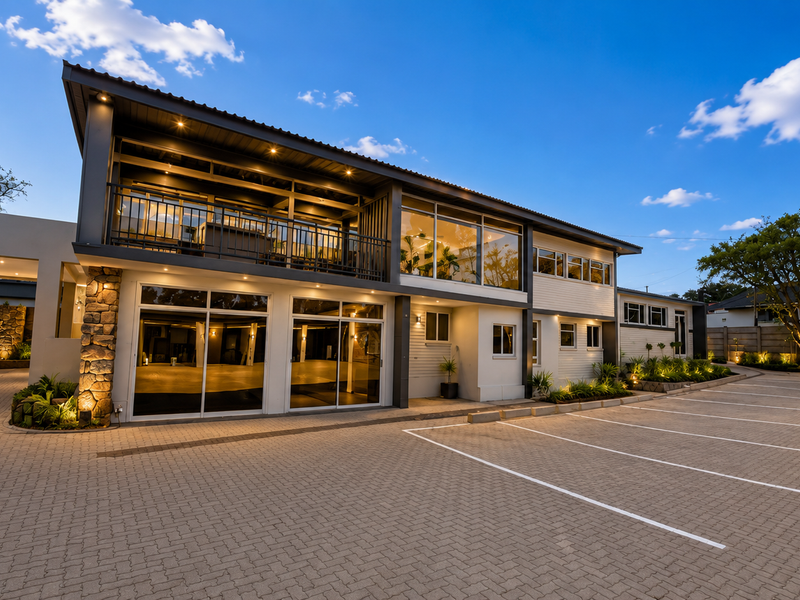 Modern office building exterior featuring a paved parking area, stone-clad accents, a spacious balcony, and integrated architectural lighting.