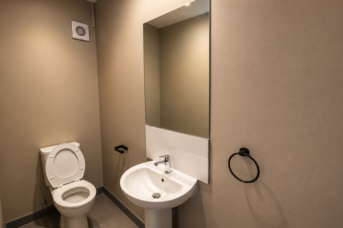 A clean, modern office restroom featuring a pedestal sink, wall-mounted mirror, and standard toilet fixture with neutral wall finishes.