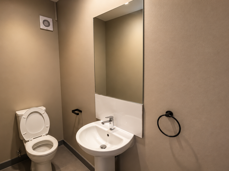 A clean, modern office restroom featuring a pedestal sink, wall-mounted mirror, and standard toilet fixture with neutral wall finishes.