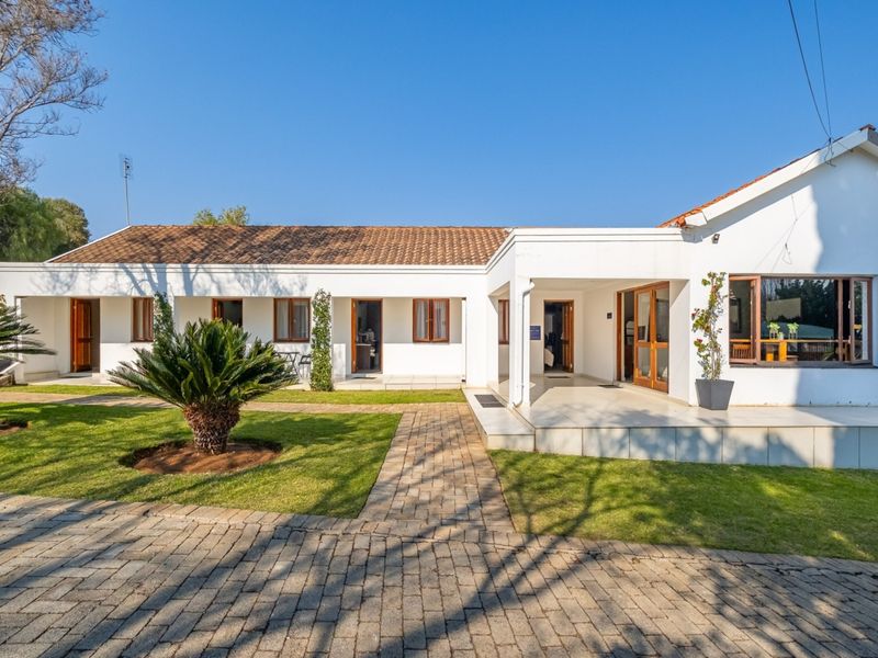A well-maintained single-story guest house exterior featuring a tiled roof, paved driveway, and a covered patio area set within a landscaped garden.