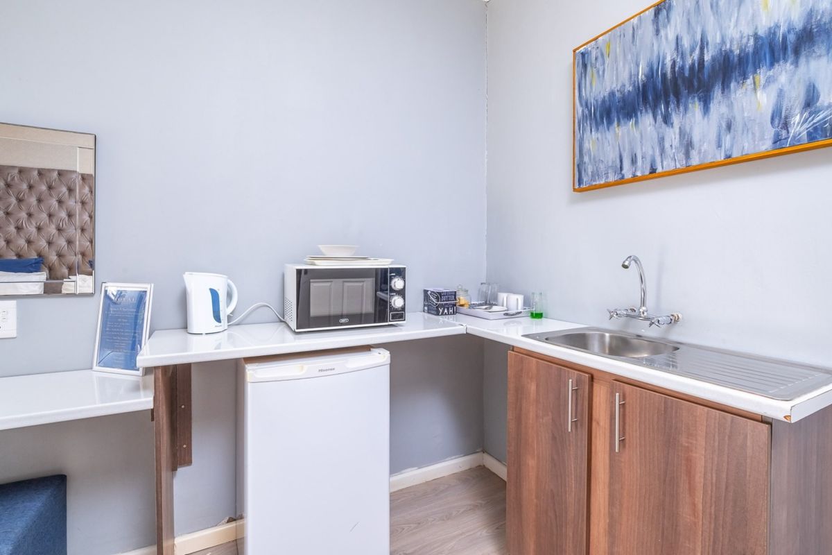 A compact kitchenette area featuring a stainless steel sink, laminate cabinetry, and a built-in microwave, suitable for guest house accommodation.
