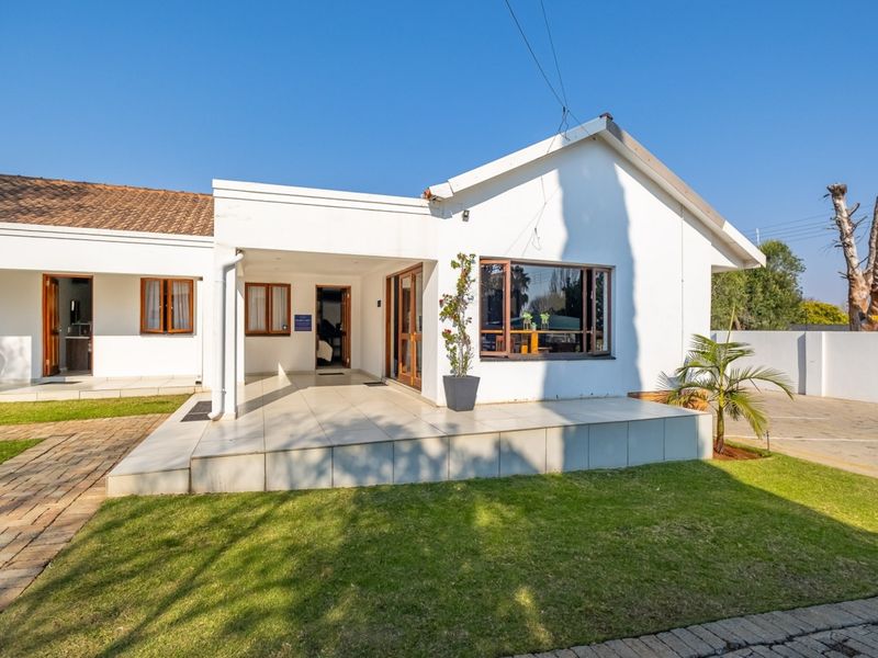 Front elevation of the guest house featuring a covered tiled patio, paved driveway, and well-maintained garden area.