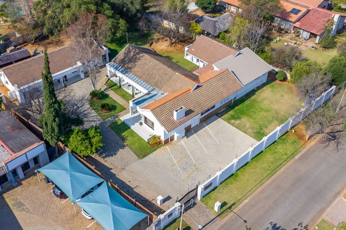 Aerial view of the guest house property featuring a tiled roof, extensive paved parking area, shade cloth carports, and established garden grounds.