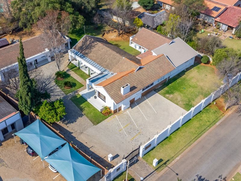 Aerial view of the guest house property featuring a tiled roof, extensive paved parking area, shade cloth carports, and established garden grounds.