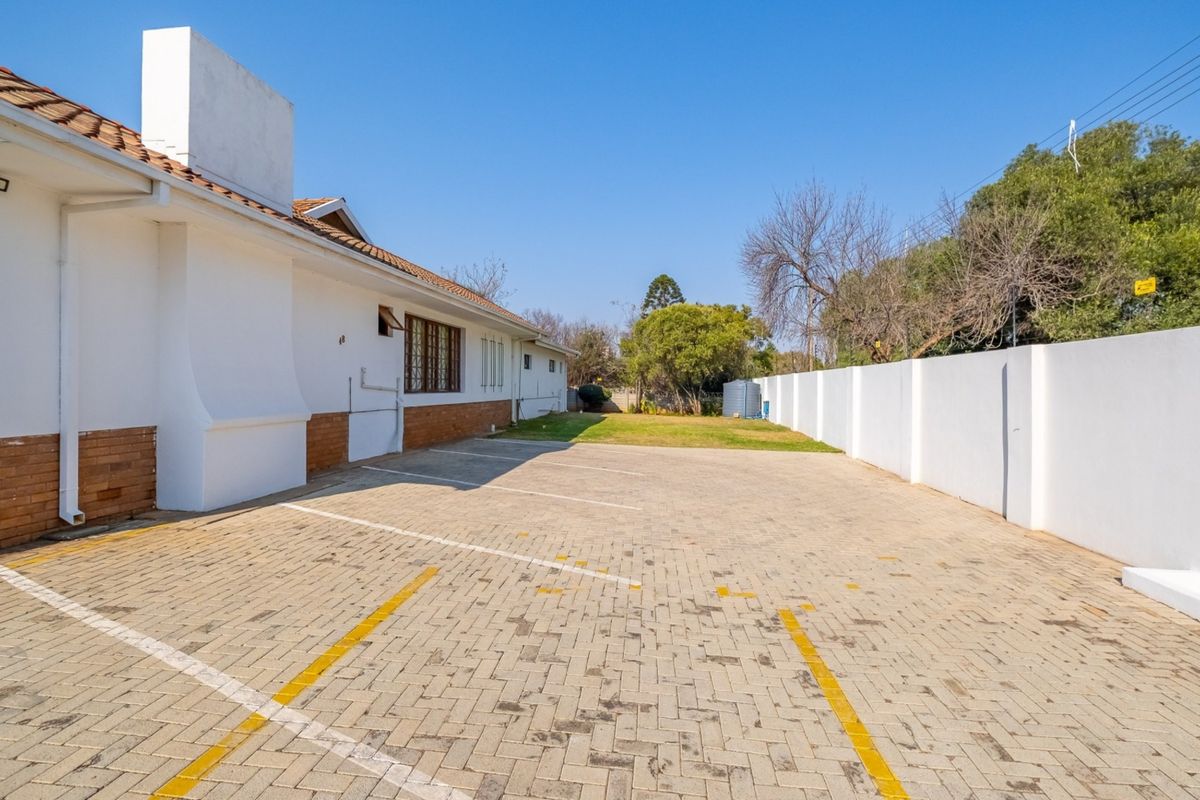 Rear exterior view of the guest house featuring a paved parking area, boundary walls, and established garden space.