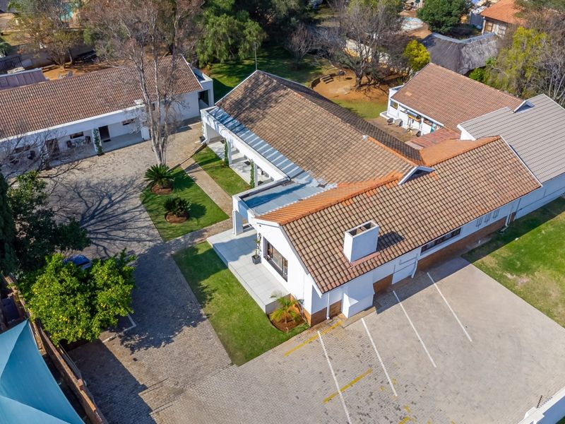 Aerial view of the guest house property featuring multiple buildings, extensive paved parking areas, and well-maintained garden grounds.