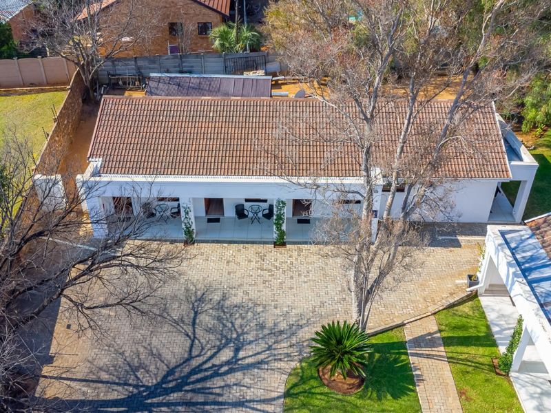 Aerial view of the guest house property featuring a tiled roof, extensive paved driveway, and a covered patio area set within a landscaped garden.