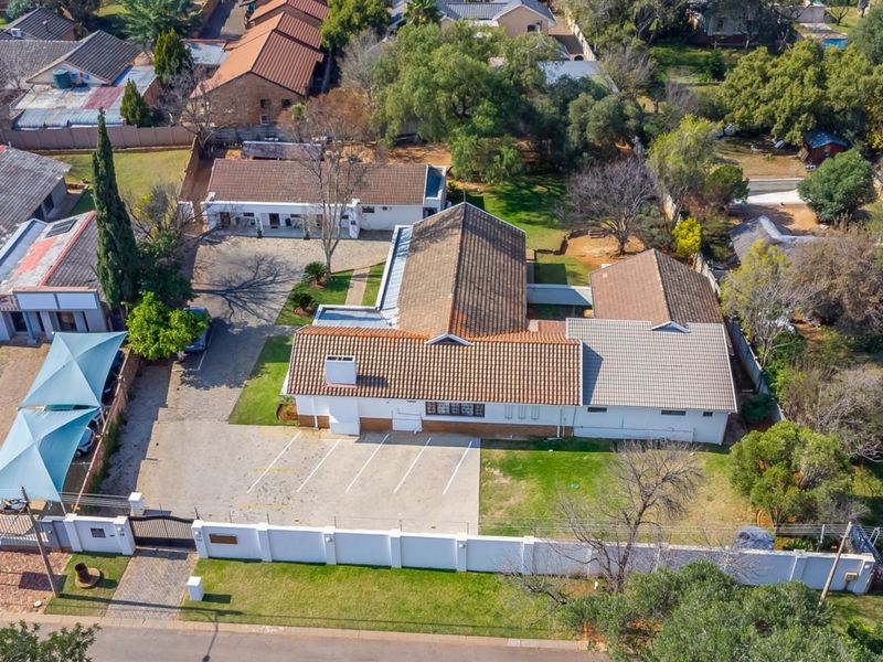 Aerial view of the guest house property featuring a large tiled roof building, paved parking area, and secure perimeter walling.