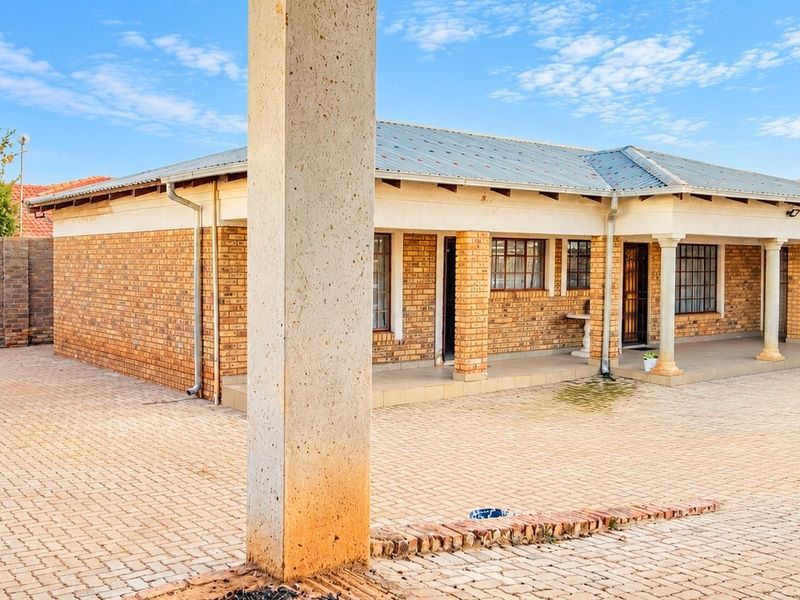 A spacious rear courtyard featuring a paved surface, covered patio area with concrete pillars, and a classic brick exterior finish.