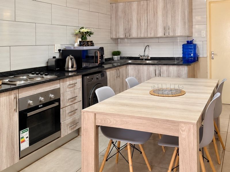 Modern kitchen featuring light wood-grain cabinetry, granite countertops, built-in oven and hob, and tiled finishes throughout.