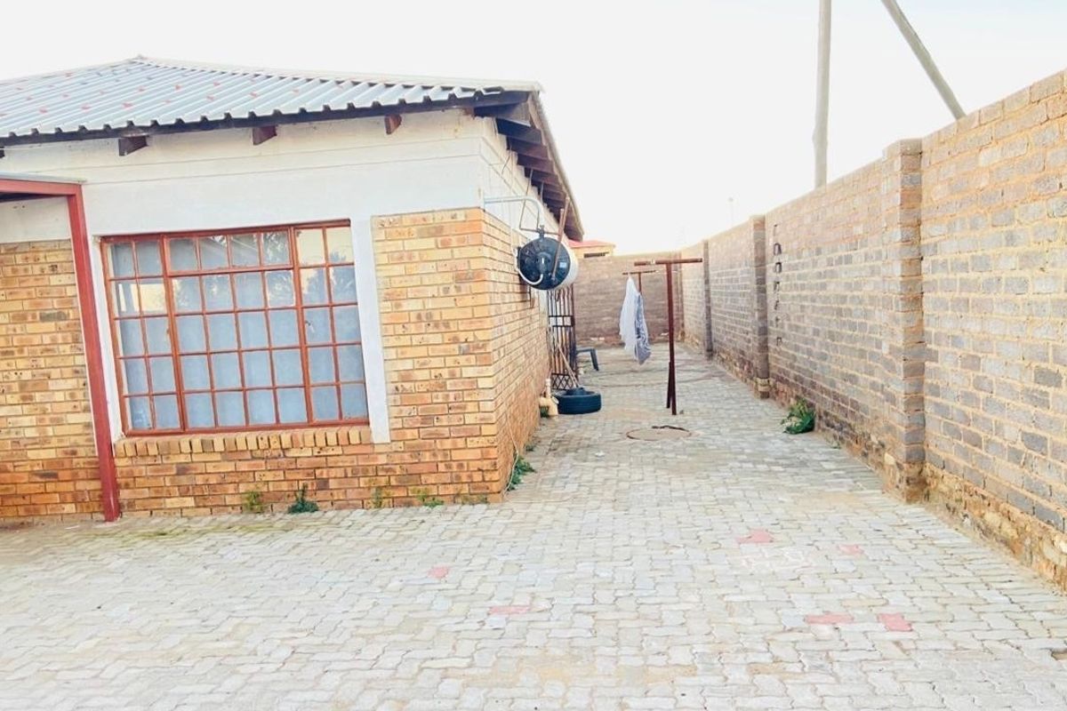 A side view of the property featuring face brick exterior walls, a paved walkway, and a secure perimeter wall.
