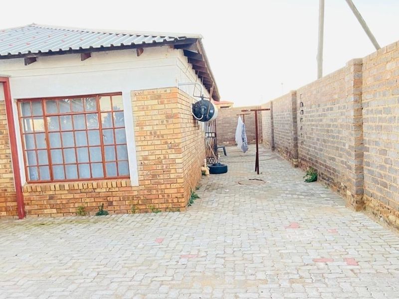 A side view of the property featuring face brick exterior walls, a paved walkway, and a secure perimeter wall.