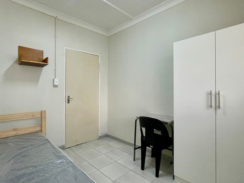 A functional bedroom featuring tiled flooring, a built-in wardrobe, and neutral wall finishes, providing a clean and simple living space.