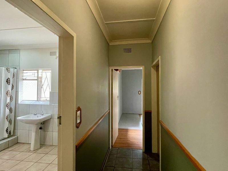 A view of a hallway leading to a bathroom featuring a pedestal basin and shower enclosure with tiled flooring and neutral wall finishes.