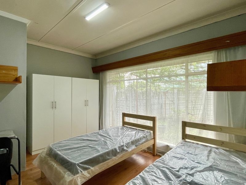 A functional bedroom featuring laminate flooring, a large window providing natural light, and a built-in wardrobe for storage.