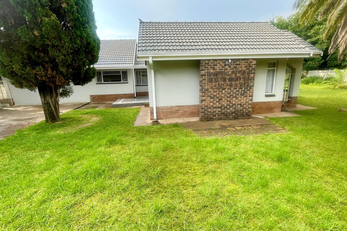 Rear view of the property featuring a tiled roof, brick chimney detail, and a concrete patio area overlooking the garden.