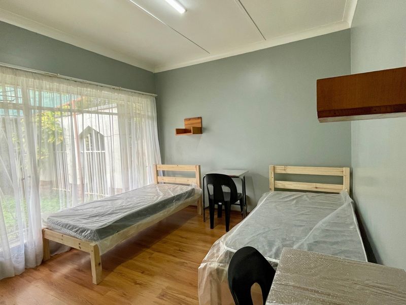 A functional bedroom featuring laminate flooring, built-in wall shelving, and a large sliding glass door providing natural light and garden access.