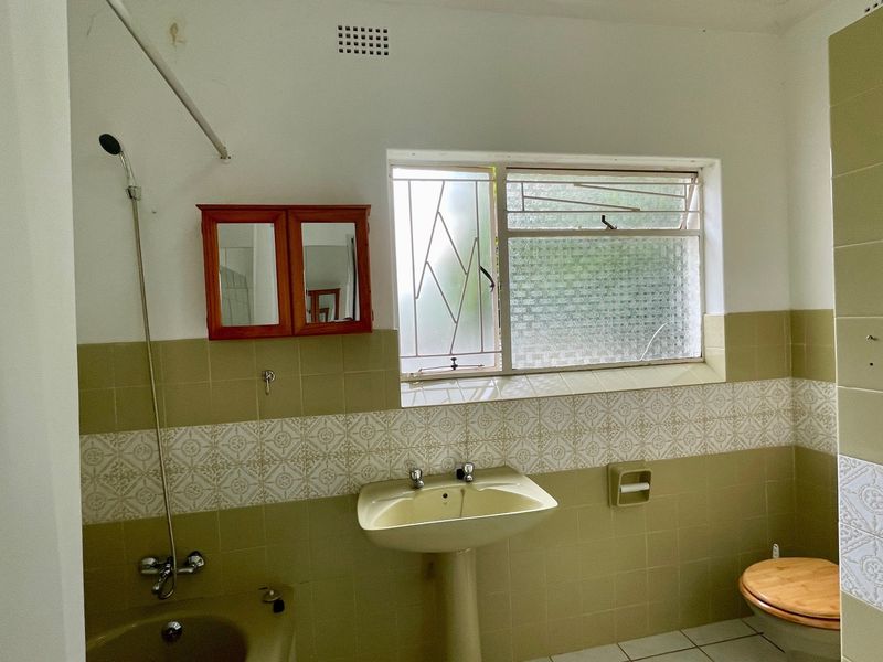 A dated bathroom featuring original pedestal basin, toilet, and tiled walls, offering significant potential for a modern renovation.