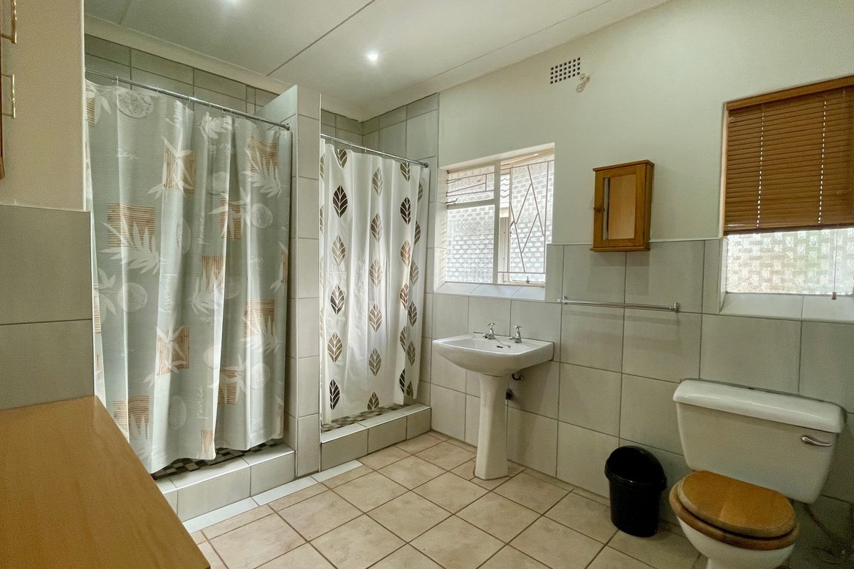 A functional bathroom featuring a pedestal washbasin, toilet, and a tiled shower area with neutral wall and floor tiles.
