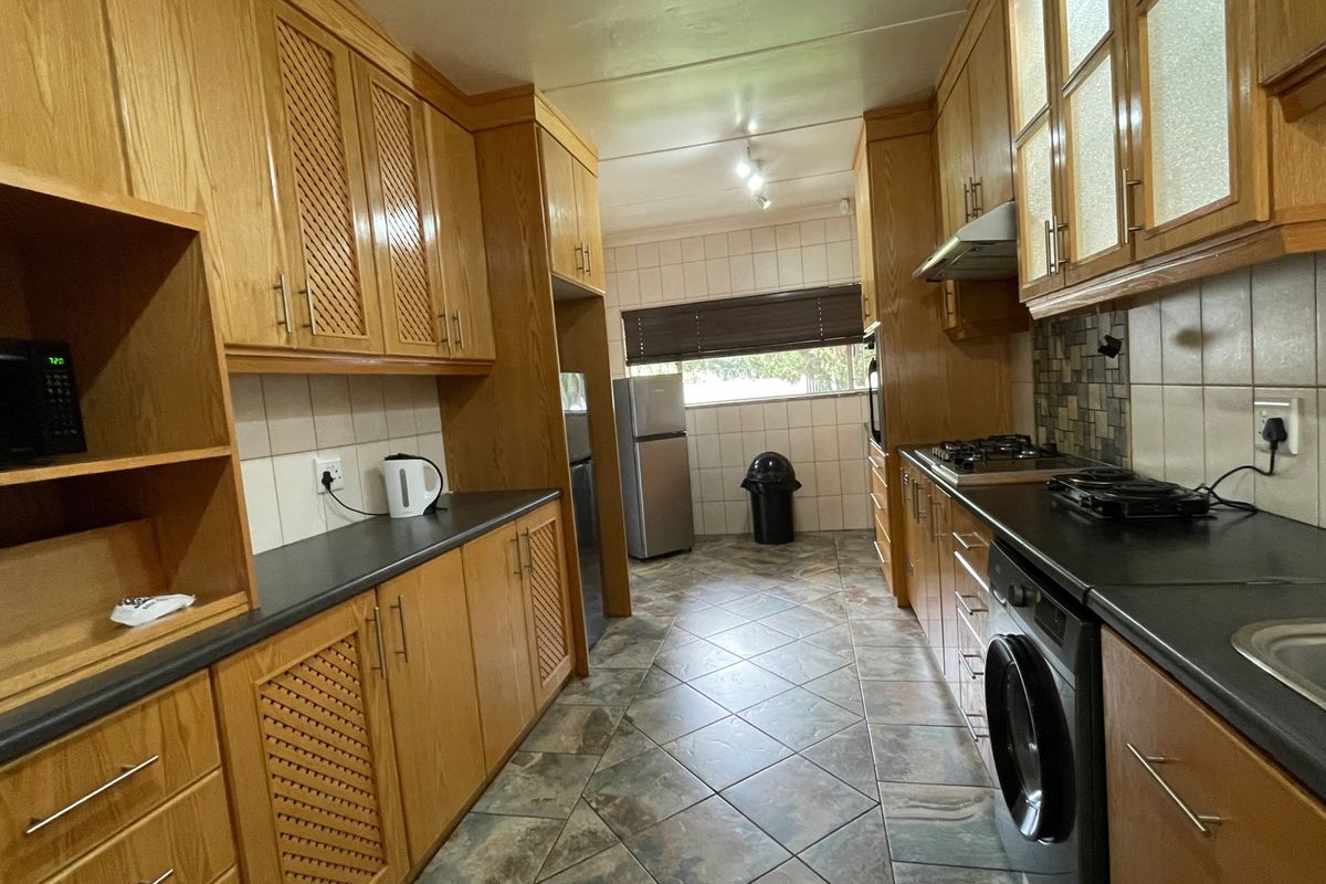 A functional galley-style kitchen featuring extensive wooden cabinetry, dark laminate countertops, tiled backsplash, and integrated appliances including a gas hob and oven.
