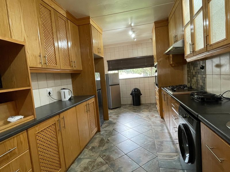A functional galley-style kitchen featuring extensive wooden cabinetry, dark laminate countertops, tiled backsplash, and integrated appliances including a gas hob and oven.