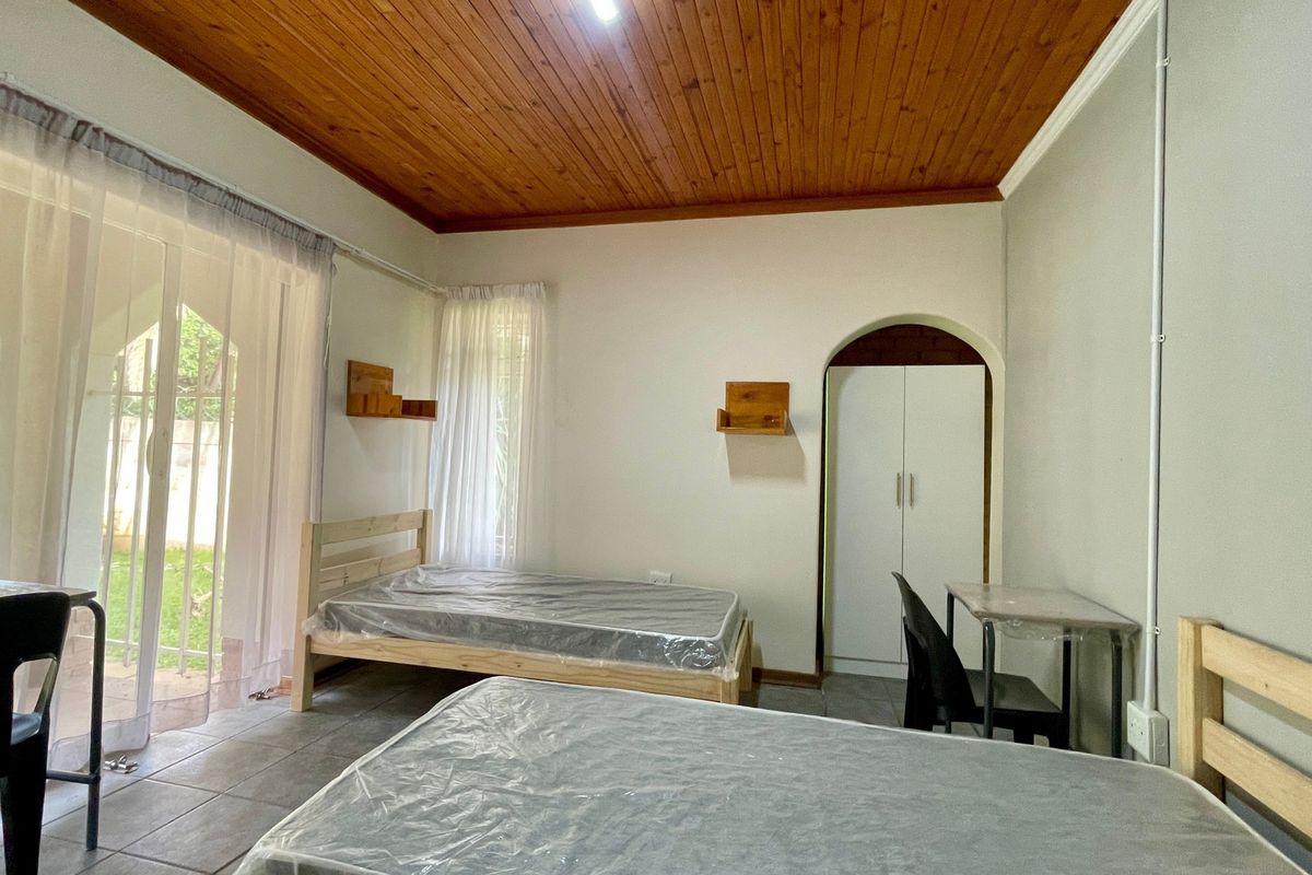 A bedroom featuring tiled flooring, a timber ceiling, and a built-in wardrobe, with direct access to the garden through a sliding glass door.
