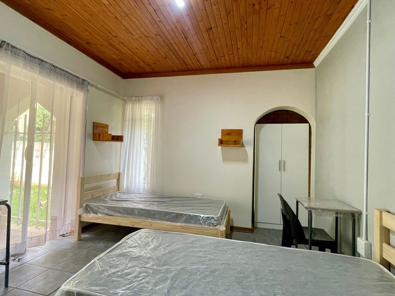 A bedroom featuring tiled flooring, a timber ceiling, and a built-in wardrobe, with direct access to the garden through a sliding glass door.