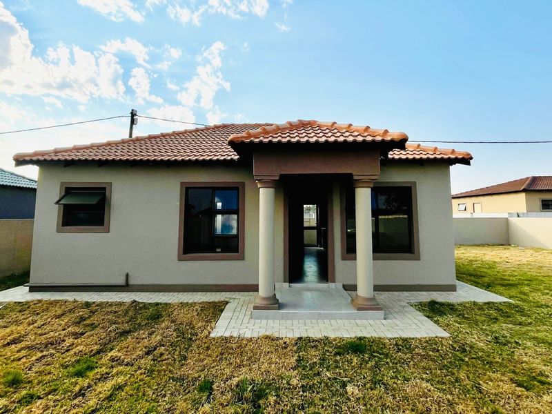 A well-maintained single-story townhouse featuring a tiled roof, decorative entrance columns, and a paved walkway set within a private yard.