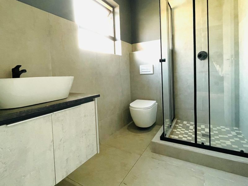 Modern bathroom featuring a sleek vessel sink on a floating vanity, wall-hung toilet, and a spacious walk-in shower with contemporary black framing.