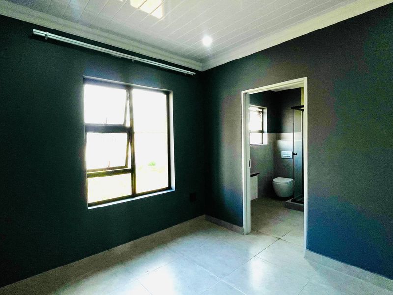 A vacant bedroom featuring dark painted walls, tiled flooring, and a tongue and groove ceiling, with direct access to an en-suite bathroom.