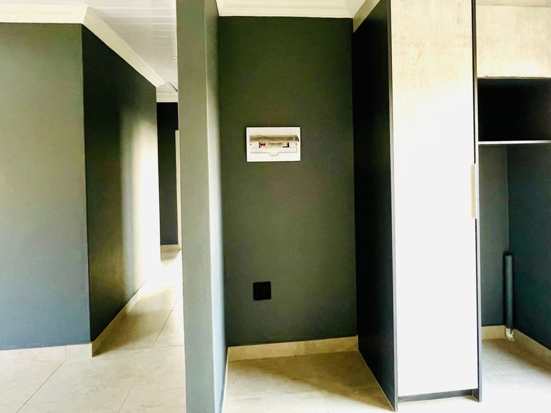 A clean, modern hallway featuring tiled flooring, dark accent walls, and built-in cabinetry with an integrated electrical distribution board.