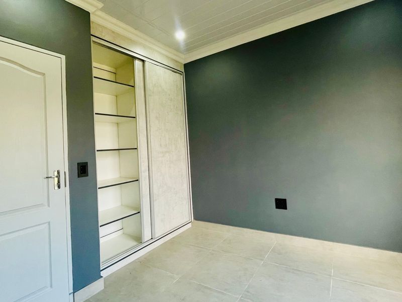A clean, empty bedroom featuring modern grey walls, tiled flooring, and a built-in sliding door wardrobe with integrated shelving.