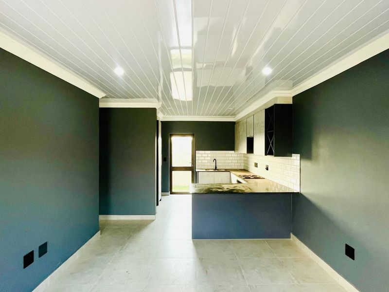 A modern, empty kitchen featuring dark cabinetry, a subway tile backsplash, stone countertops, and a clean, minimalist aesthetic with recessed lighting.